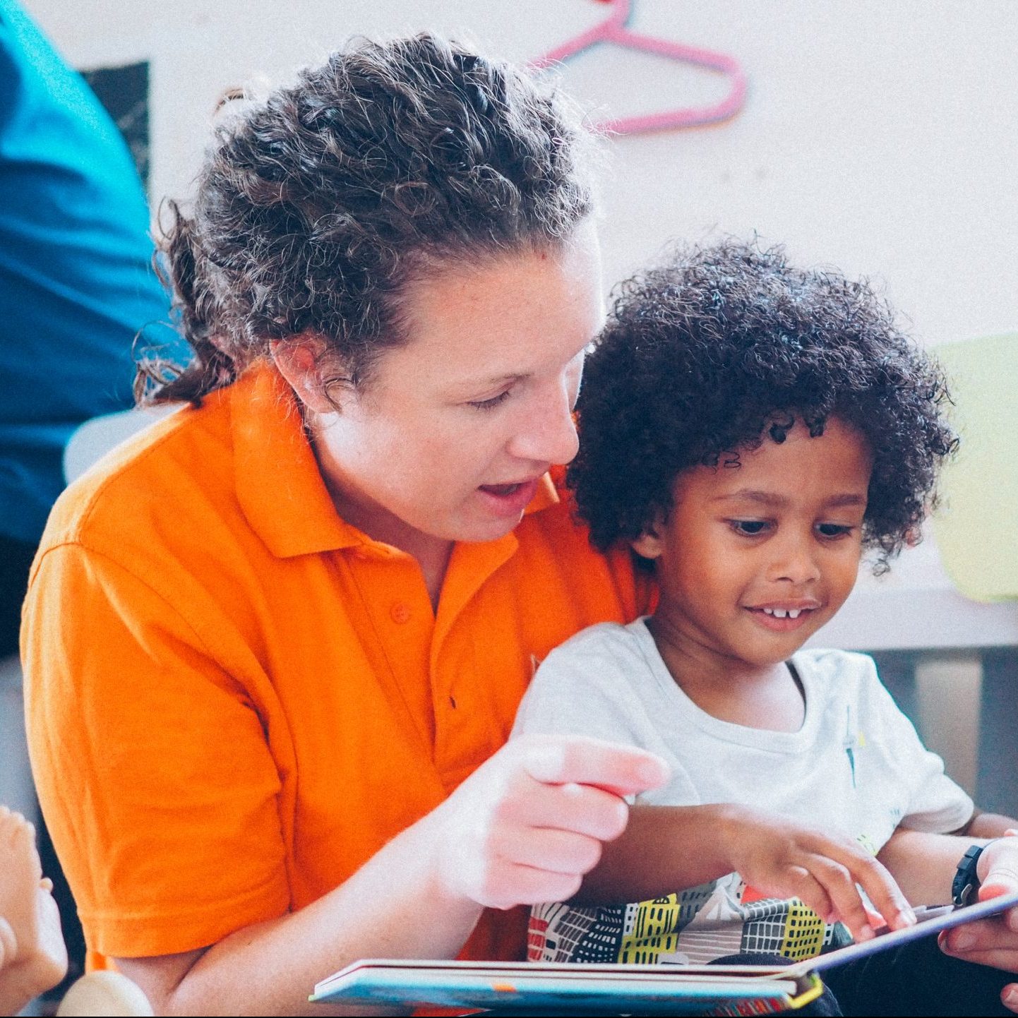 woman in an orange tshirt reading a book to a young child sitting on her lap