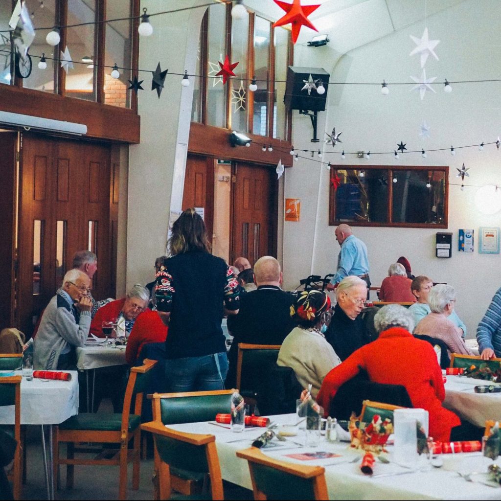 A group of people sitting around tables in a space decorated for Christmas