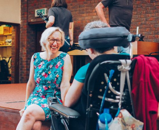 A lady sitting with a blue dress laughing looking at a lady in a wheelchair